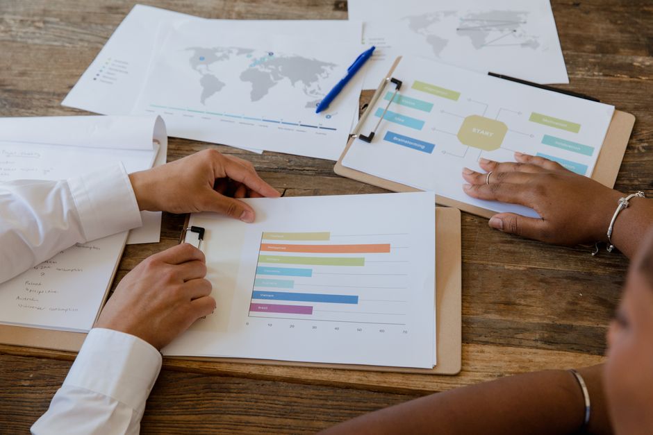 Gestão de Crise Online — Top view of colleagues discussing charts and graphs on a wooden table during a business meeting.